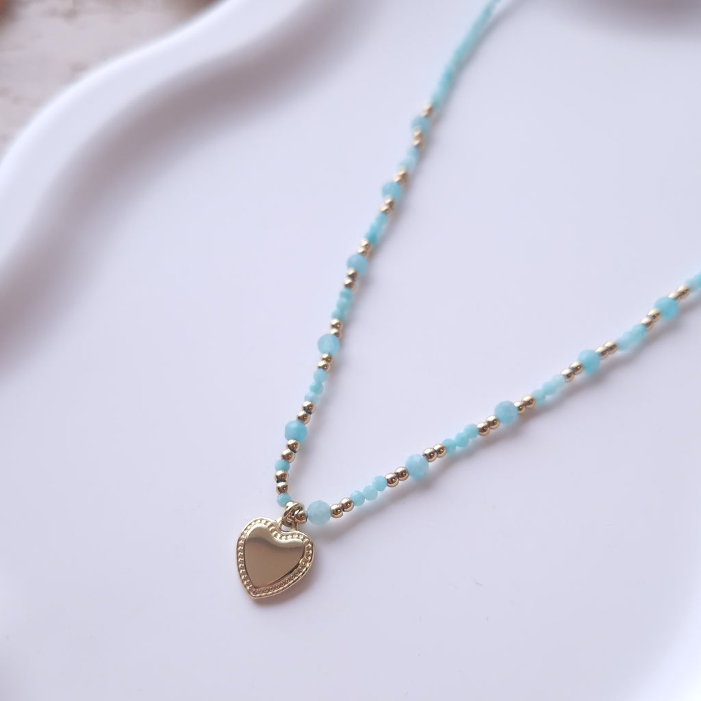 détail collier perles bleues ras du cou avec pendentif coeur en acier inoxydable bijou fin et élégant femme