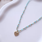 détail collier perles bleues ras du cou avec pendentif coeur en acier inoxydable bijou fin et élégant femme