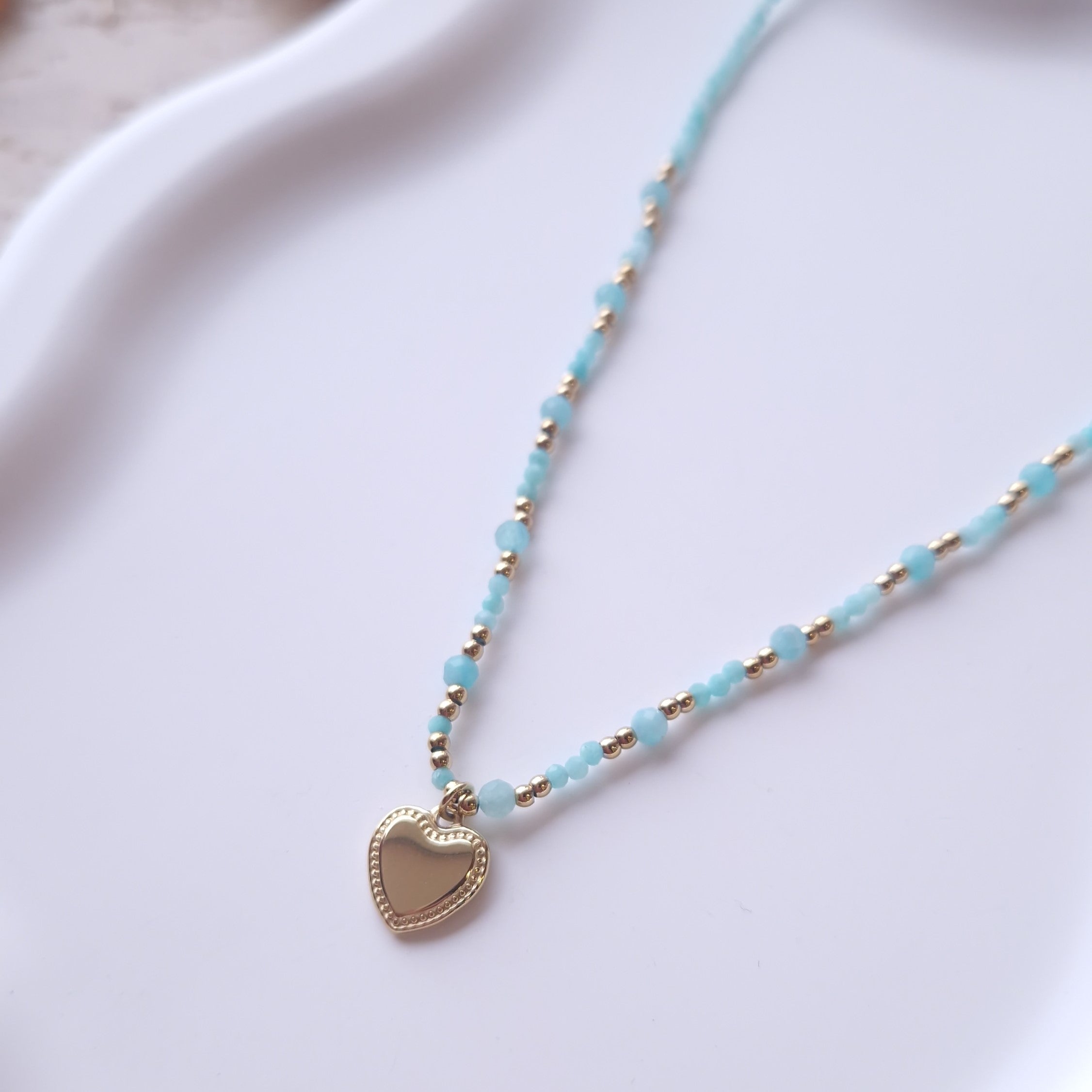 détail collier perles bleues ras du cou avec pendentif coeur en acier inoxydable bijou fin et élégant femme